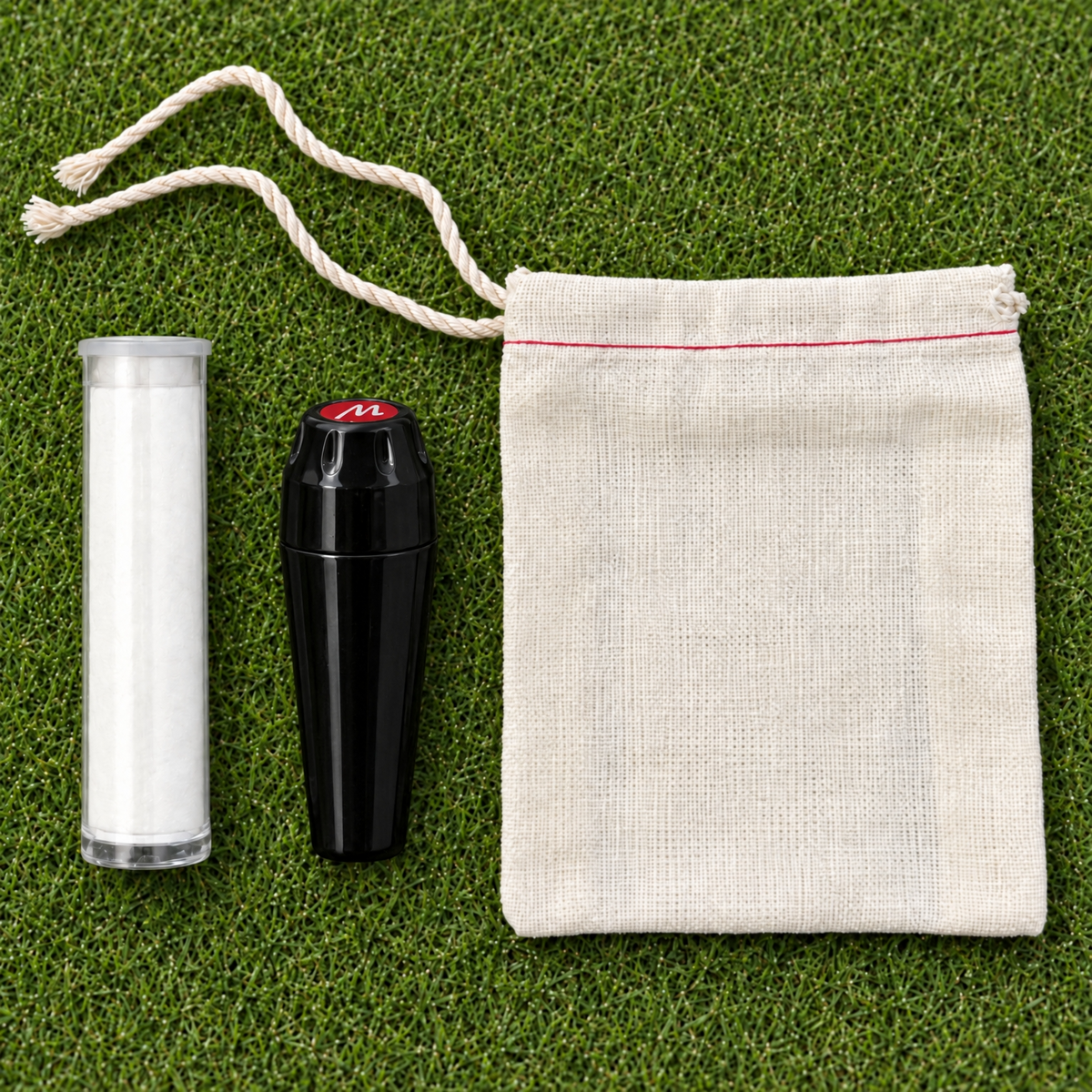 Black Marc-it marker, white powder refill tube, and cotton drawstring pouch on a putting green.